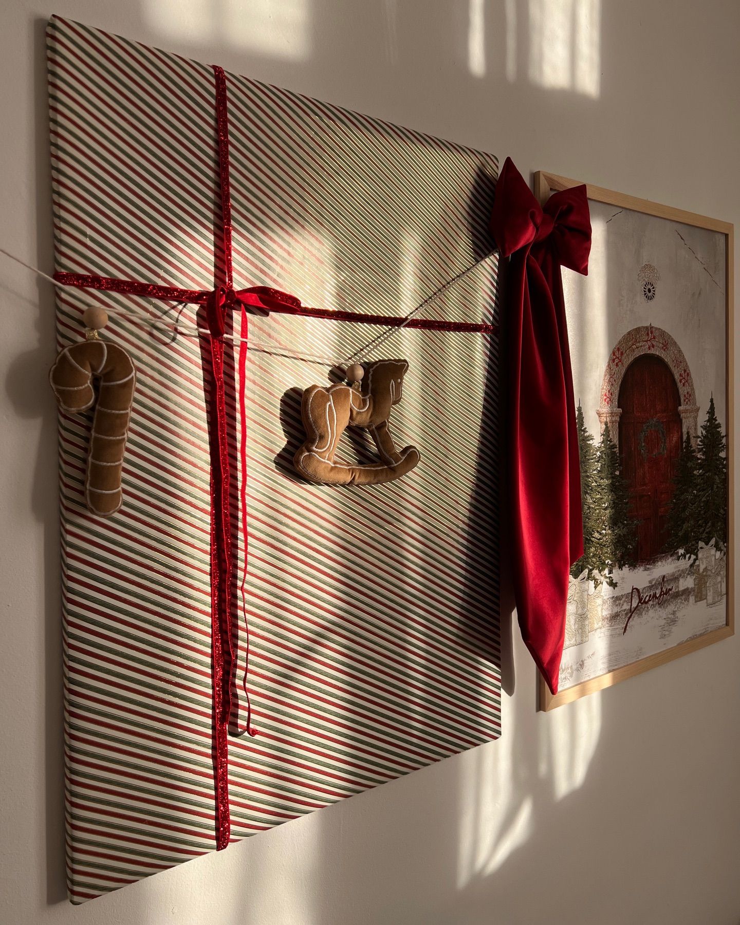A deep red fabric bow hangs beside a framed Christmas picture wrapped like a gift.