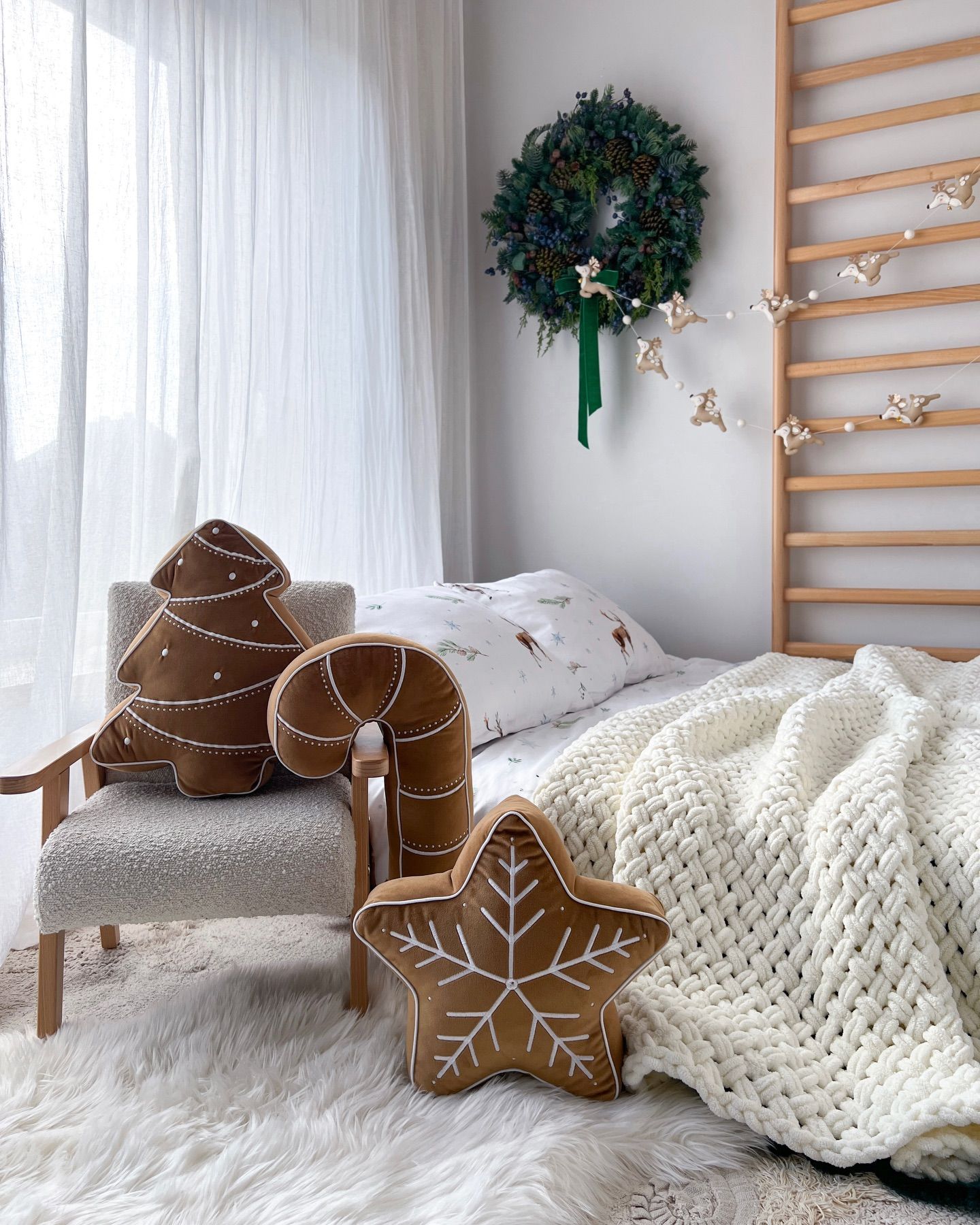 Gingerbread-shaped cushions sit on a cosy children’s bed beneath a green Christmas wreath.