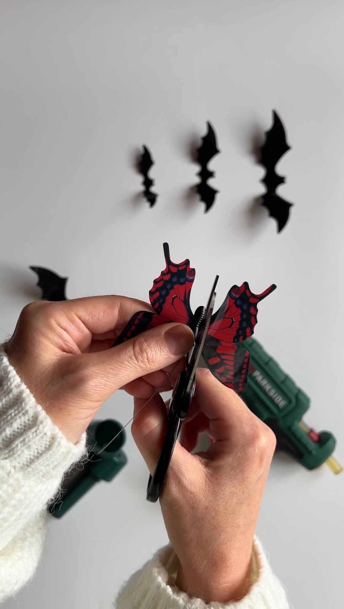 Gosia’s hands make a paper bat beside small black bats on a wall.
