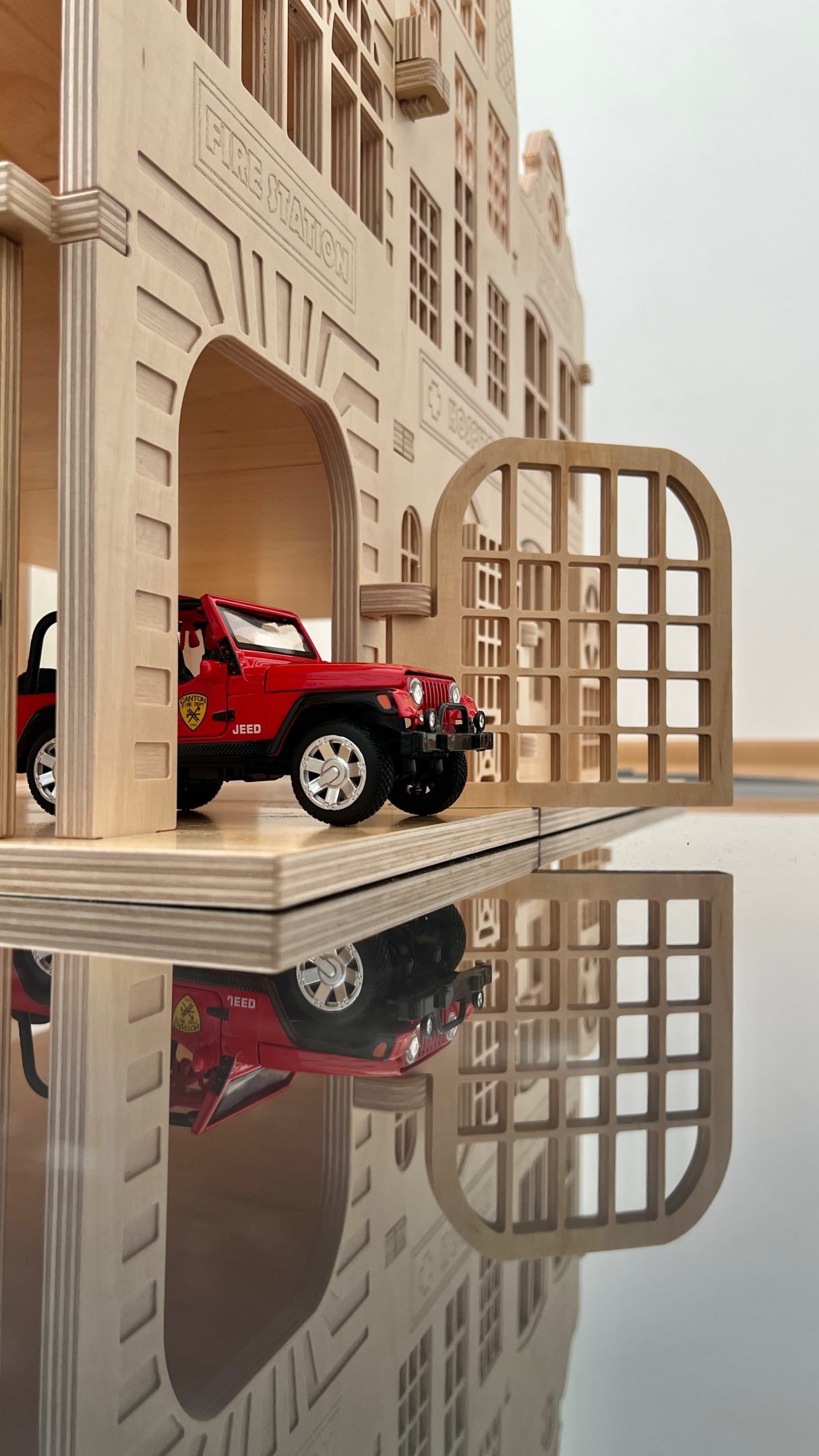 A tiny red car in an intricately made wooden toy parking garage.
